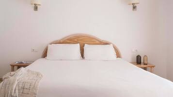 A neatly made bed with white linens, two bedside lamps, a bedside table with a book, and a small vase.