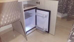 A compact refrigerator with a single door and a small freezer compartment, located in a corner of a room with a tiled floor and a patterned wall. - SunMoon (Rome)