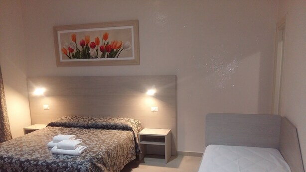 A hotel room with a large bed, a smaller bed, a nightstand, and a painting of tulips on the wall. - SunMoon (Rome)