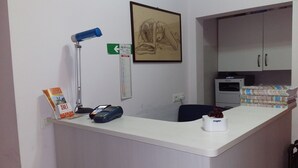 A reception desk with a desk lamp, a calendar, a framed artwork, a stack of papers, and a small vase. - SunMoon (Rome)