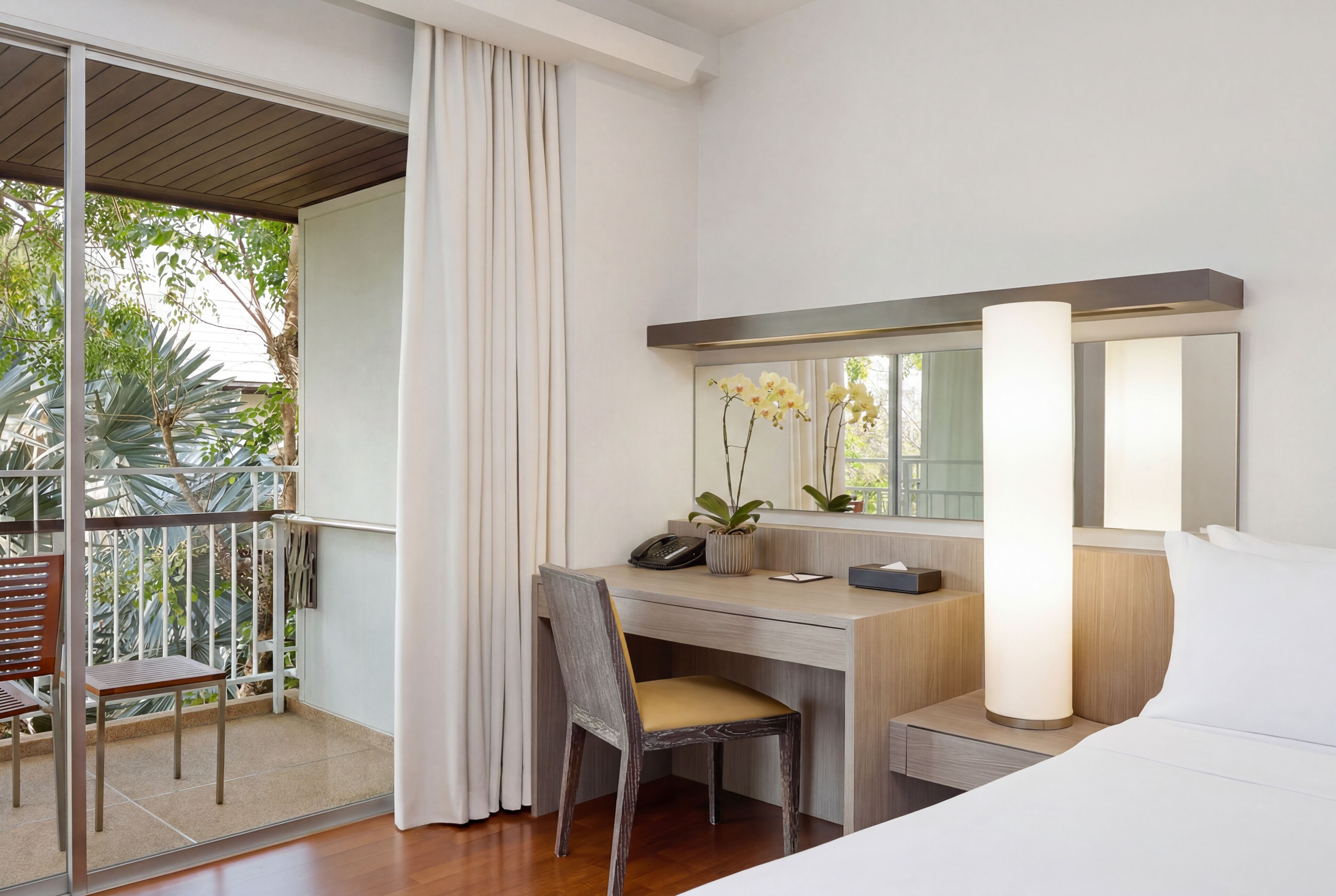 Hotelkamer met balkon, bureau met stoel, bed, grote spiegel en bedlamp.