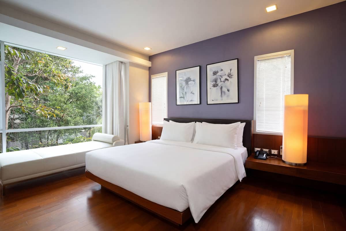 Un dormitorio moderno con una cama grande, un banco junto a la ventana y dos lámparas de pared.