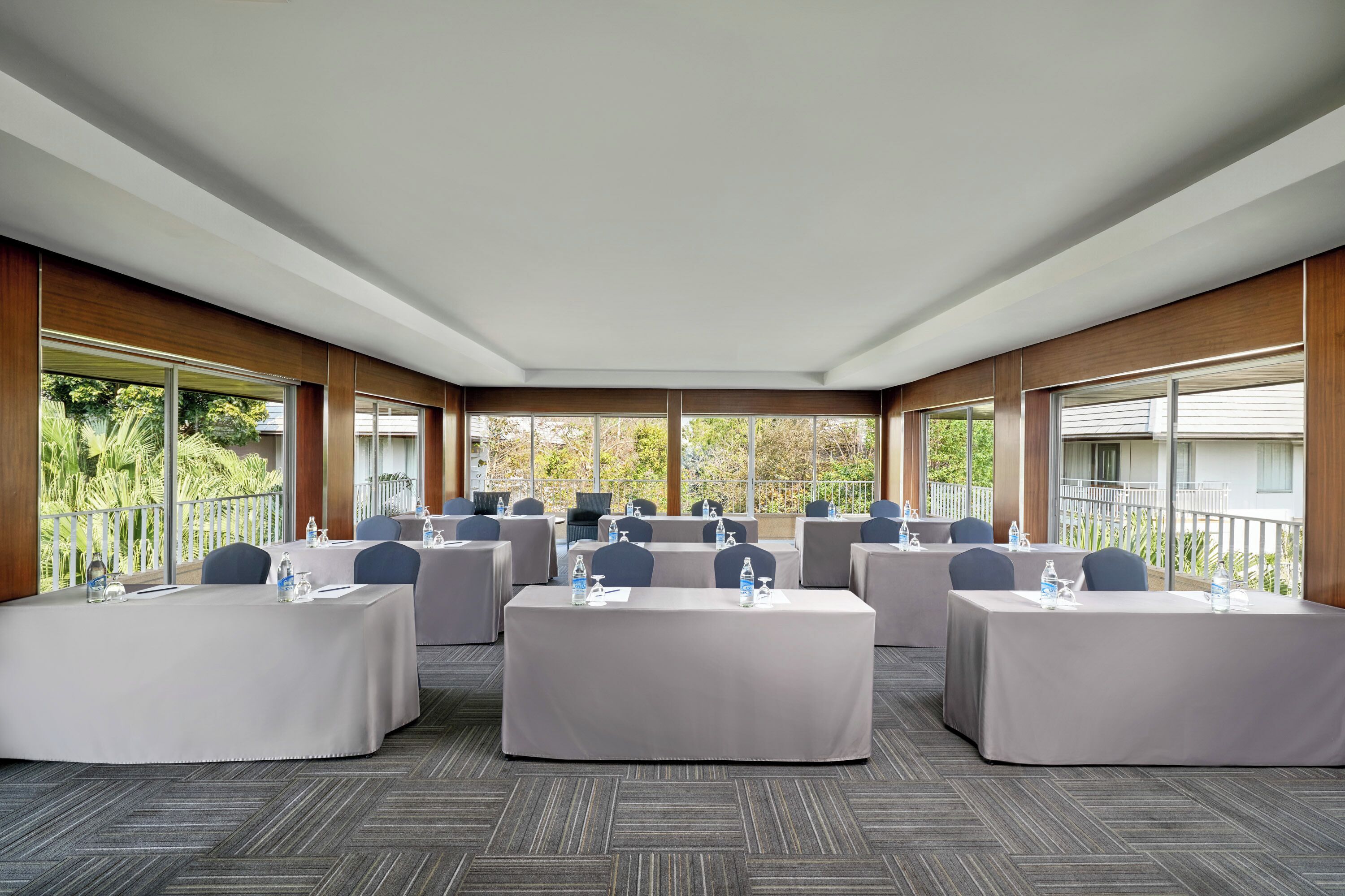 A conference room with multiple tables, chairs, and large windows offering a view of the outdoors.