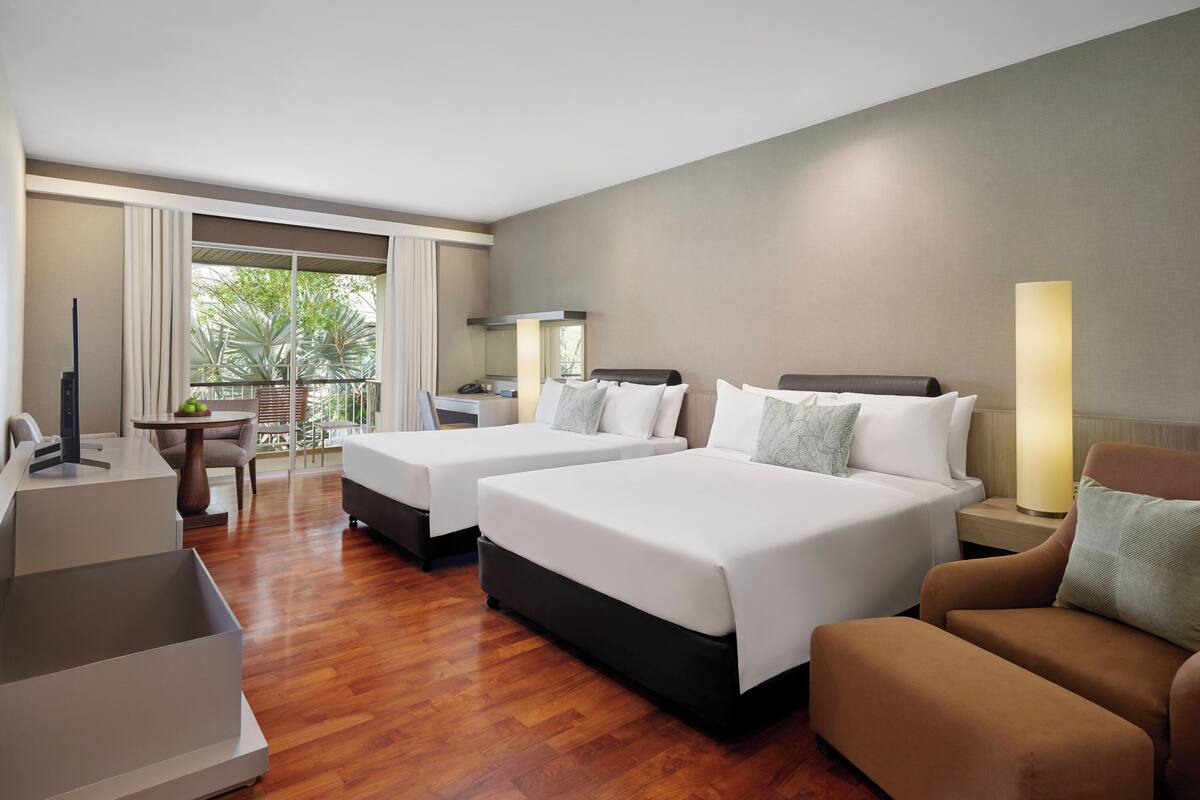 Habitación de hotel con dos camas, un escritorio, una silla, una lámpara y vistas al exterior.