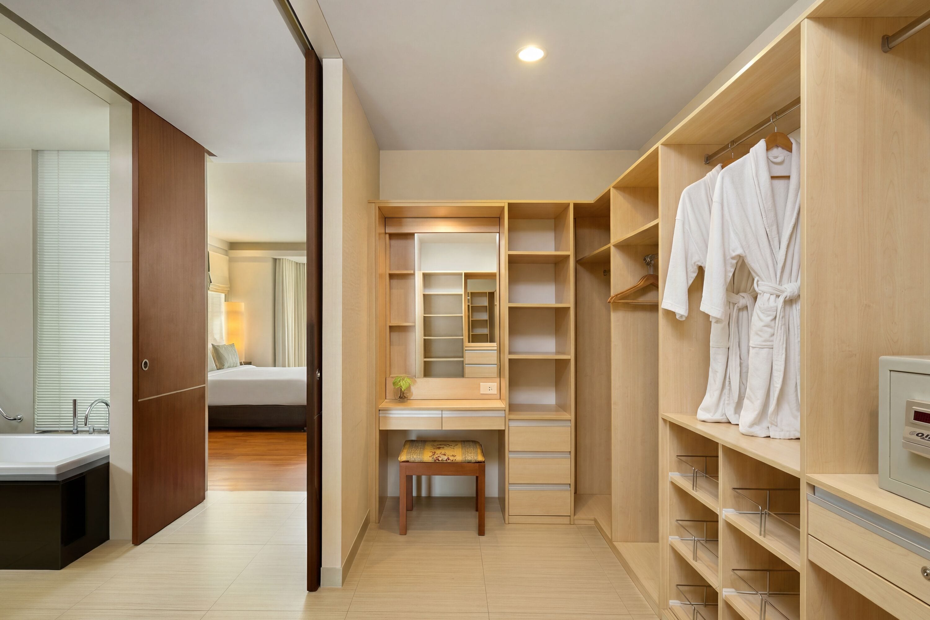 Una habitación de hotel moderna con vestidor, tocador con espejo y una cama al fondo.