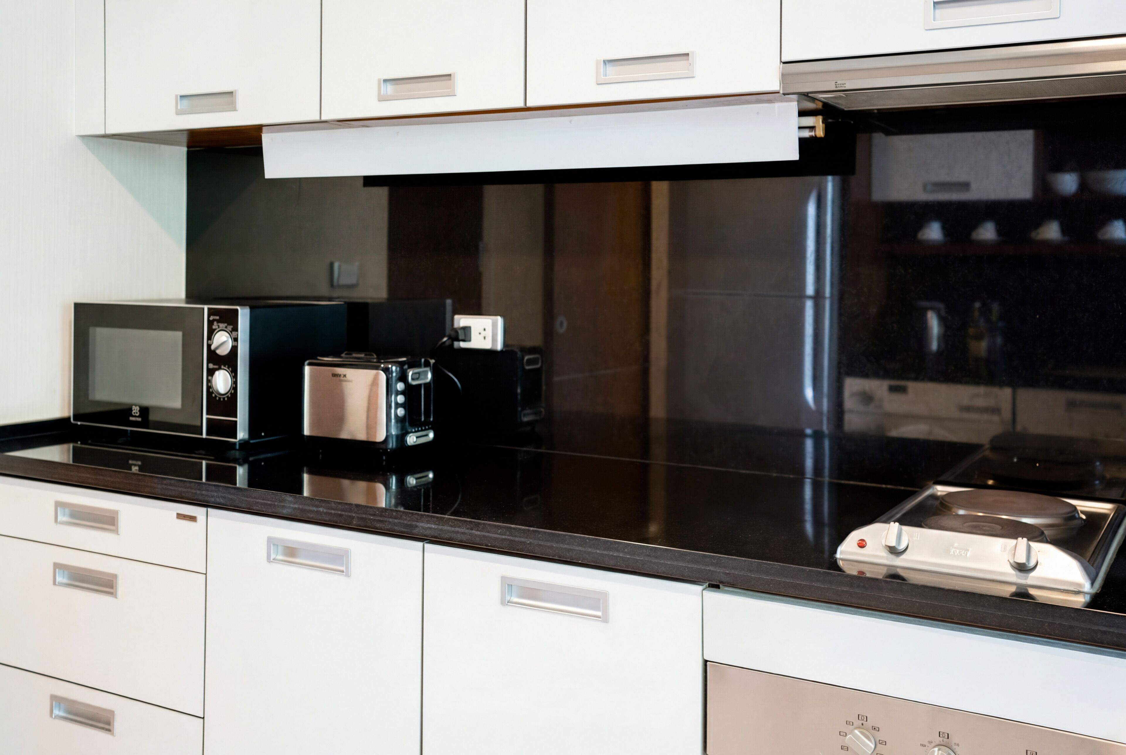 Une cuisine moderne avec des meubles blancs, un plan de travail noir, un four à micro-ondes encastré, un grille-pain et une cuisinière.