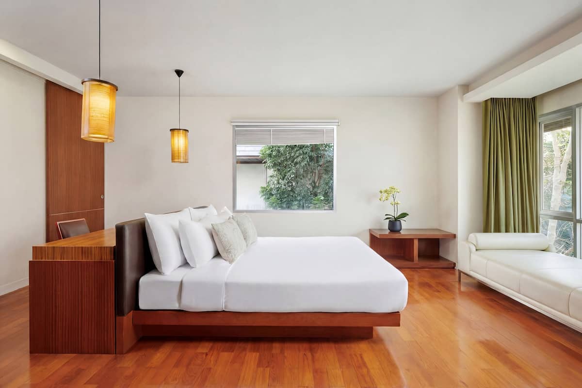 Un dormitorio moderno con un escritorio de madera, una cama con ropa de cama blanca, dos lámparas colgantes, una ventana con persianas y una cortina verde.