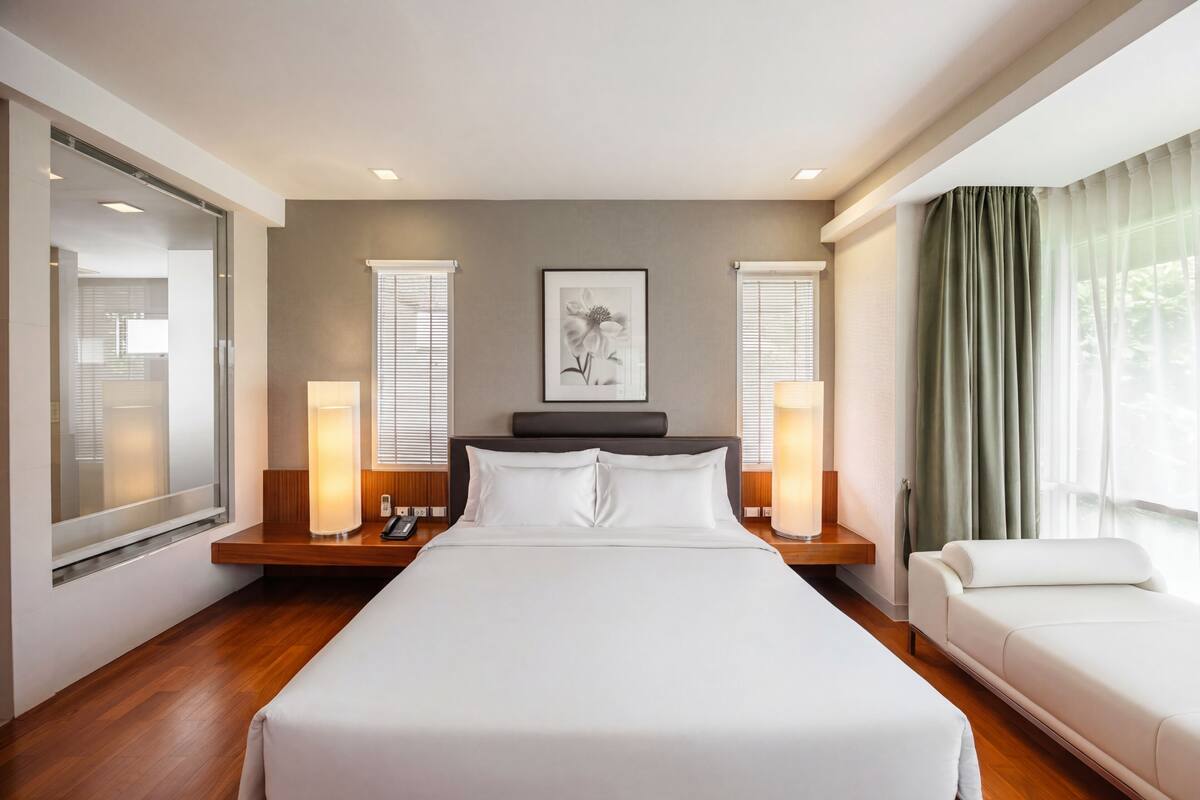 Una habitación de hotel moderna con una cama grande, lámparas de noche, una mesita de noche, una obra de arte enmarcada en la pared y vistas al exterior a través de la ventana.