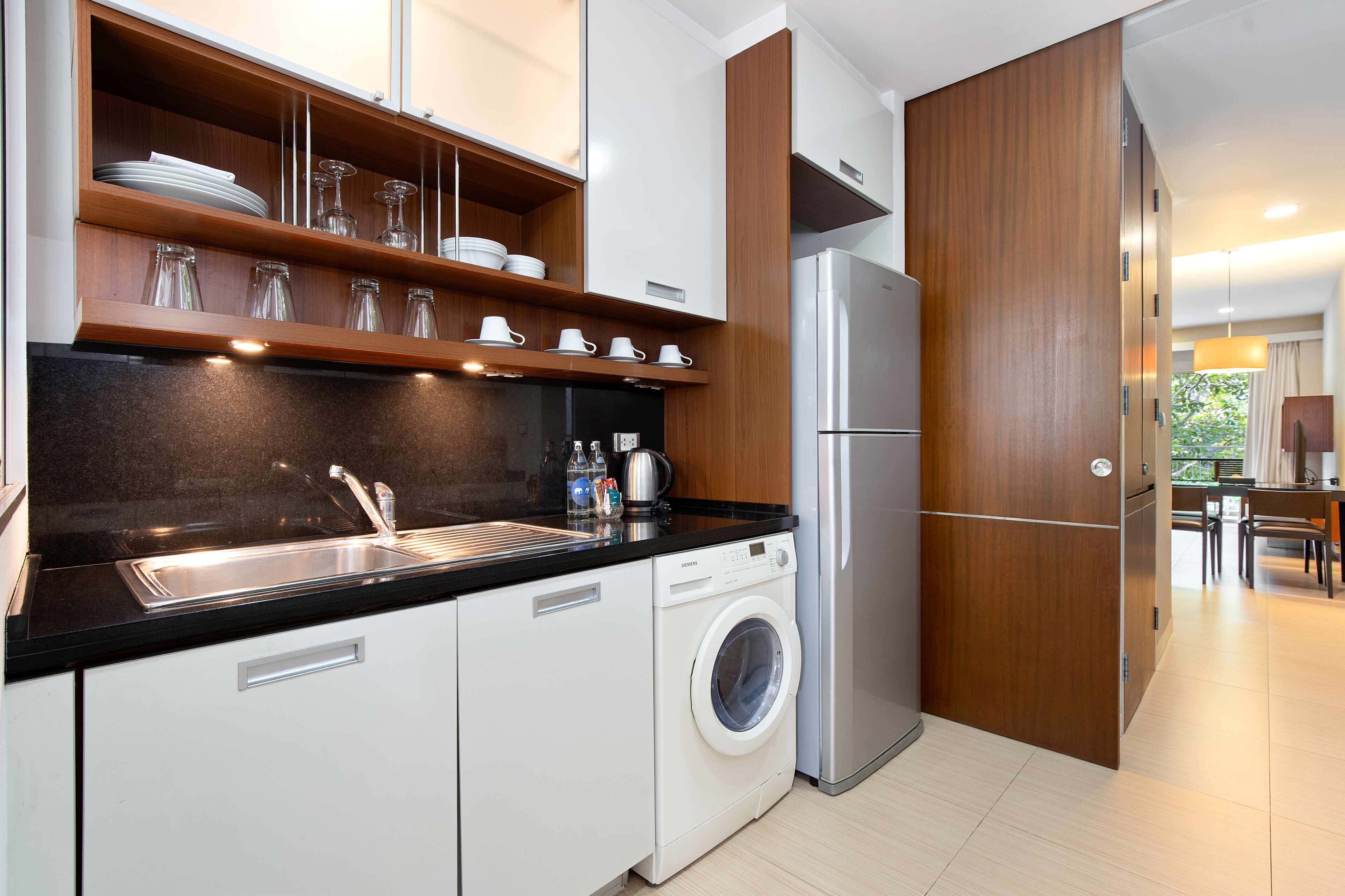 Una cocina moderna con lavadora integrada, refrigerador de acero inoxidable y repisas de madera sobre el lavamanos.