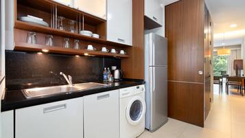 Una cocina moderna con lavadora integrada, refrigerador de acero inoxidable y repisas de madera sobre el lavamanos.