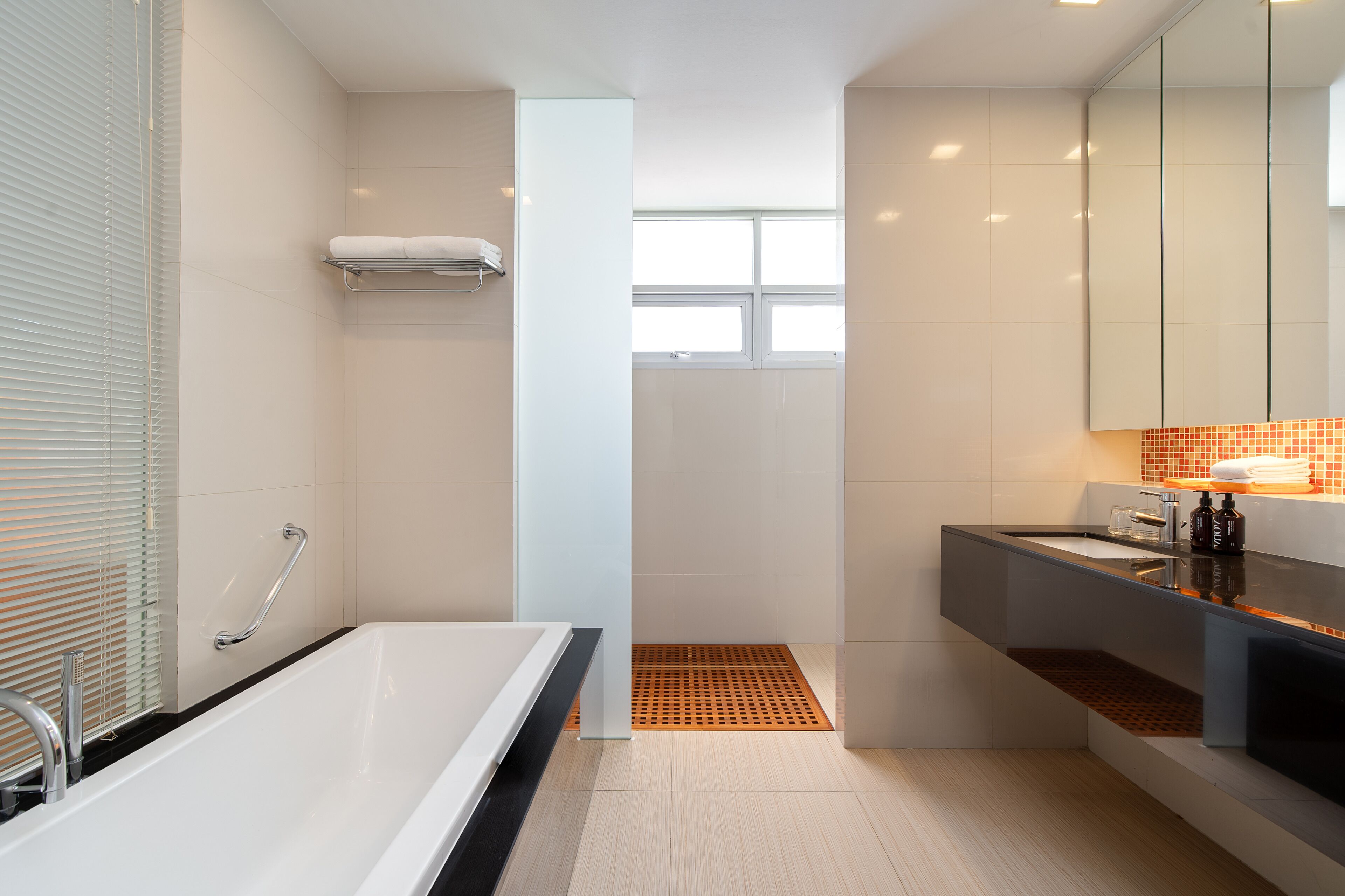 A modern bathroom with a bathtub, a shower area, a vanity with a mirror, and a window providing natural light.
