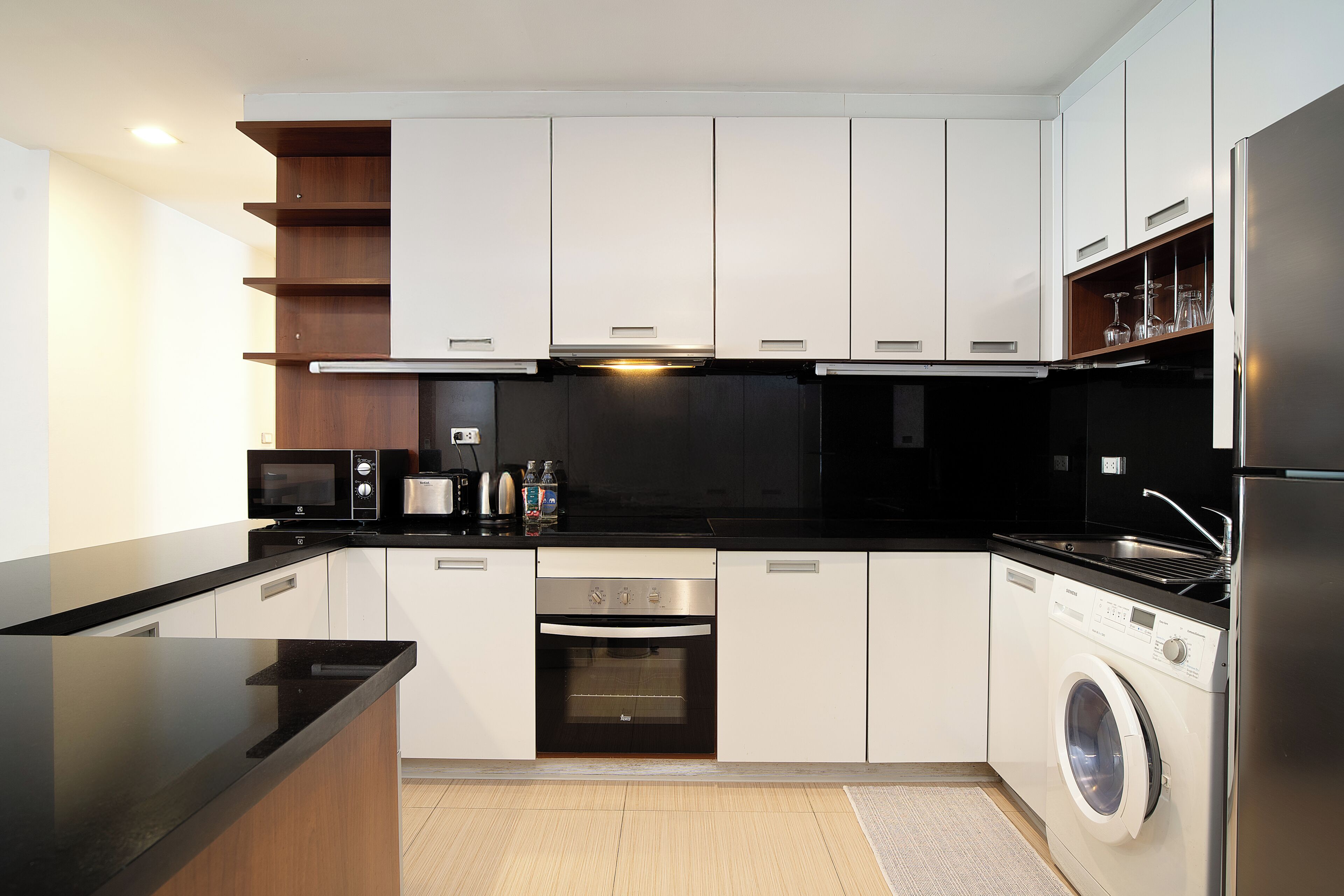 A modern kitchen with white cabinets, a black countertop, stainless steel appliances, and a built-in washing machine.