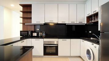 A modern kitchen with white cabinets, a black countertop, stainless steel appliances, and a built-in washing machine.