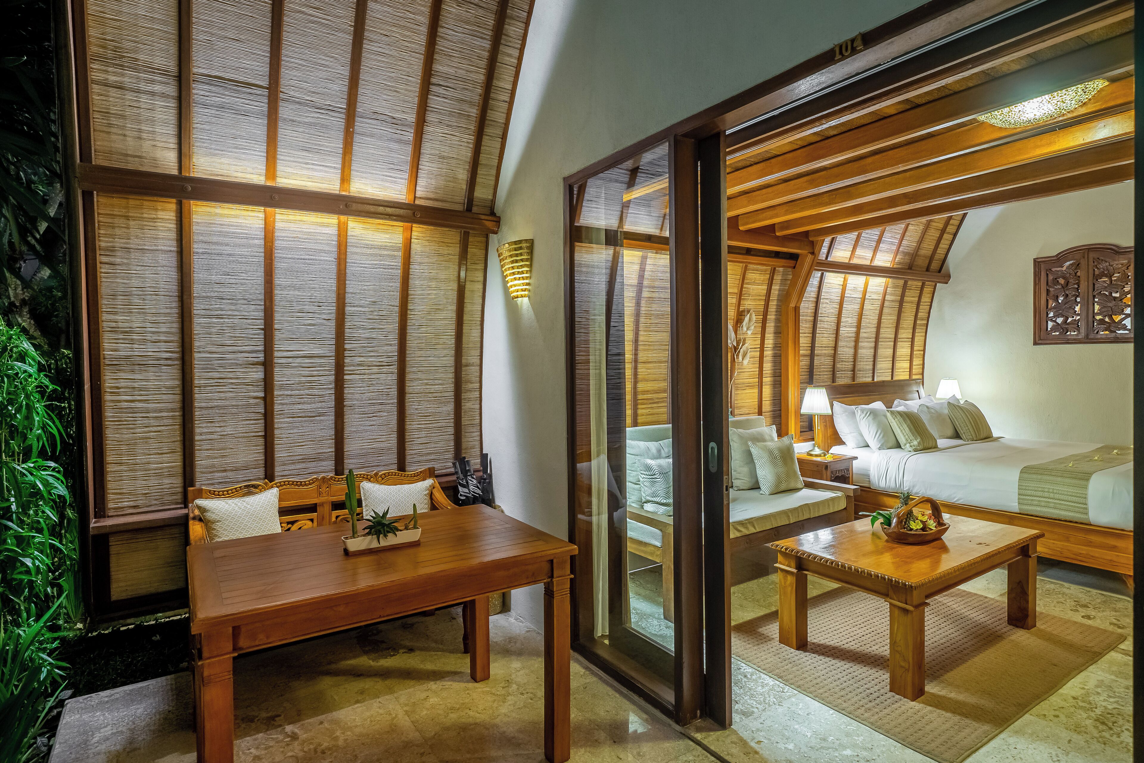 A traditional Japanese-style room with tatami flooring, a low wooden table, a sofa, and a sliding glass door leading to a bedroom with a bed and a nightstand.