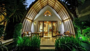A modern building with a curved roof and large windows, surrounded by lush greenery. - Klumpu Bali Resort (Denpasar)