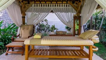 Una cama de madera con dosel, una silla y una mesa en un espacio al aire libre cubierto con plantas.