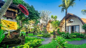 A courtyard with a traditional Balinese house, a stone pathway, and lush greenery. - Klumpu Bali Resort (Denpasar)