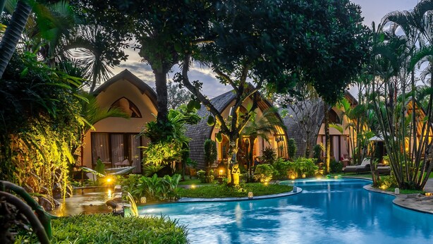 A resort with a swimming pool surrounded by lush greenery and well-lit buildings. - Klumpu Bali Resort (Denpasar)