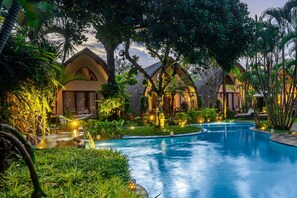 A resort with a swimming pool surrounded by lush greenery and well-lit buildings.