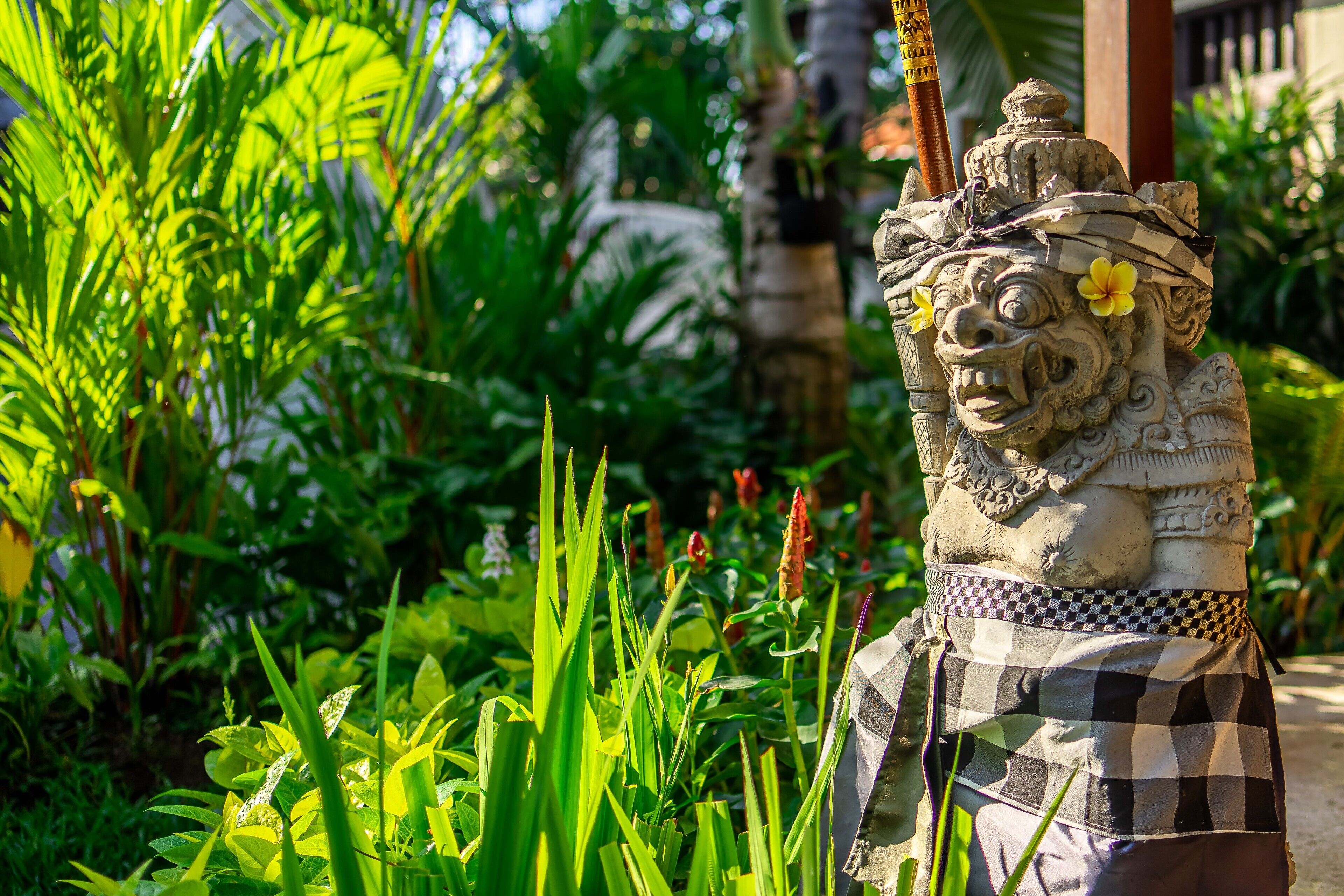 A stone statue with a checkered cloth, surrounded by lush greenery.