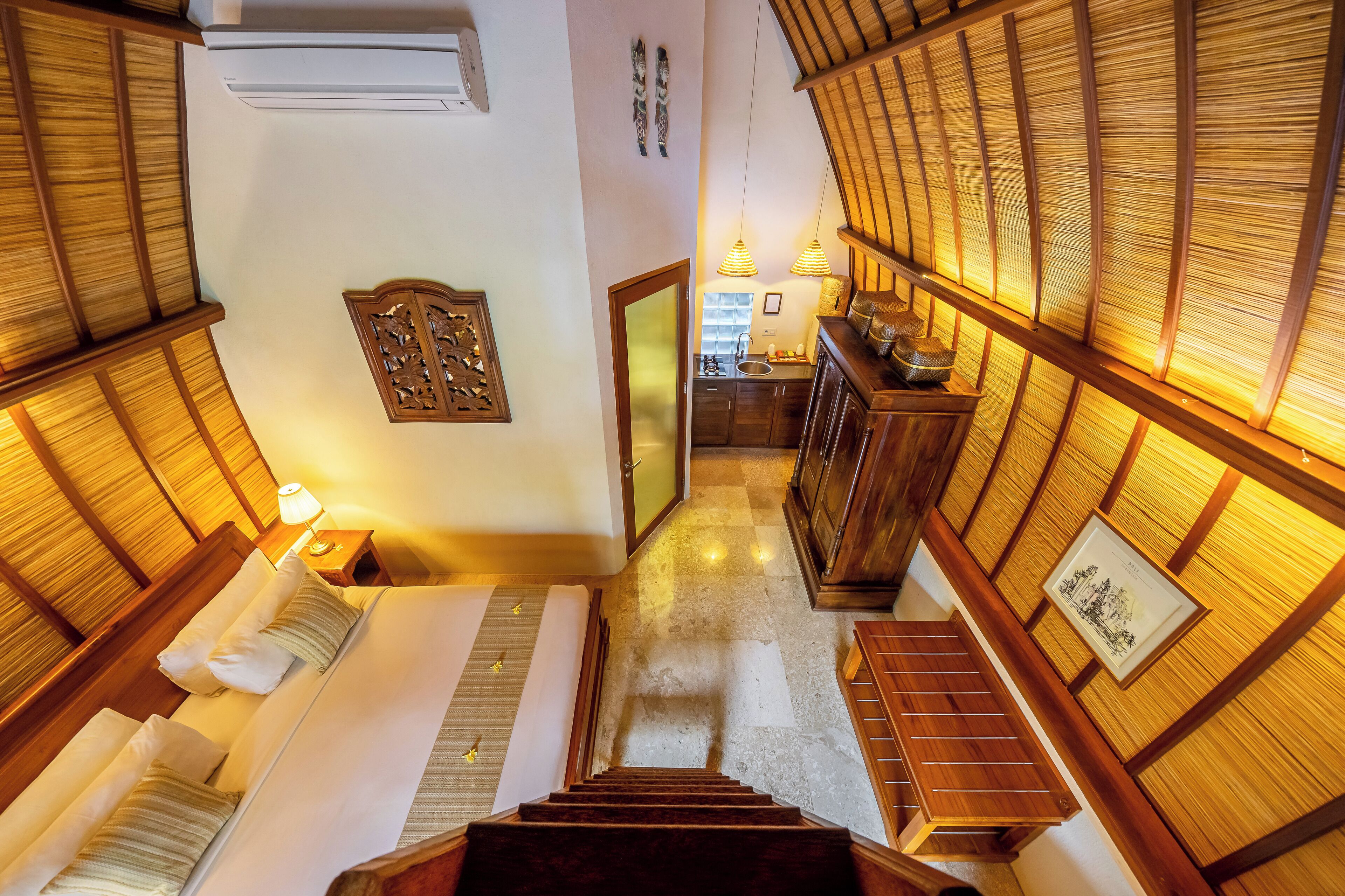 A hotel room with a wooden staircase, a bed, a nightstand, and a view of the kitchen.