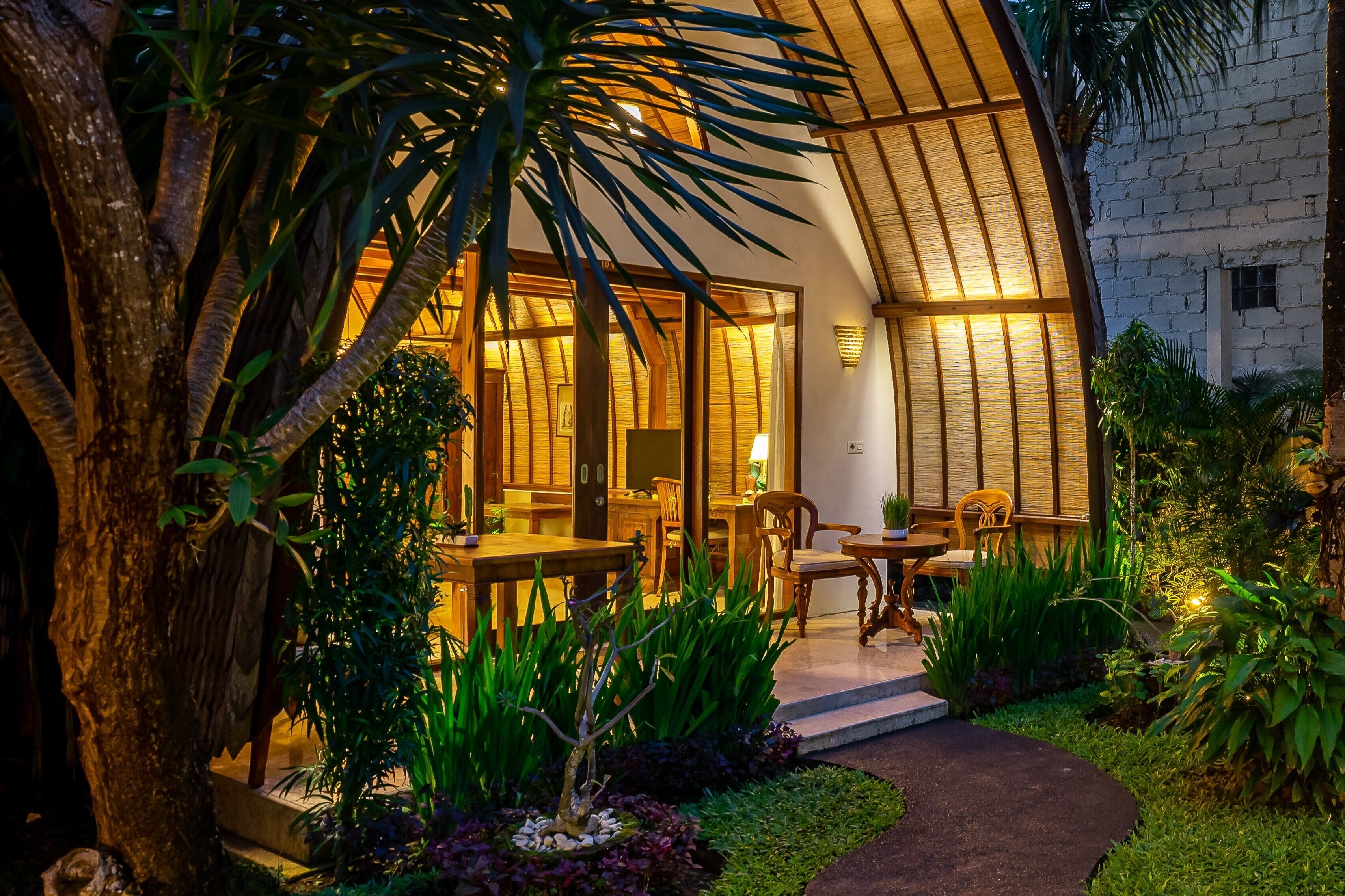 A modern building with a curved roof, wooden furniture, and a garden with tropical plants.