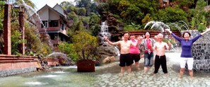 A group of people enjoying a water feature with multiple fountains, surrounded by lush greenery and a stone building. - Feng Ya Yue Zhu (Guanxi)