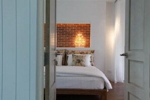 Quarto com parede de tijolos, cama com roupa de cama floral e mesa de cabeceira.