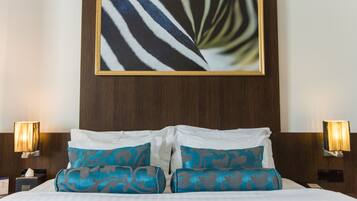 A hotel room with a large bed, two pillows, a framed artwork above the bed, and two bedside lamps.