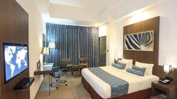 A hotel room with a large bed, a desk with a chair, a television, and a view of the outside through curtains.