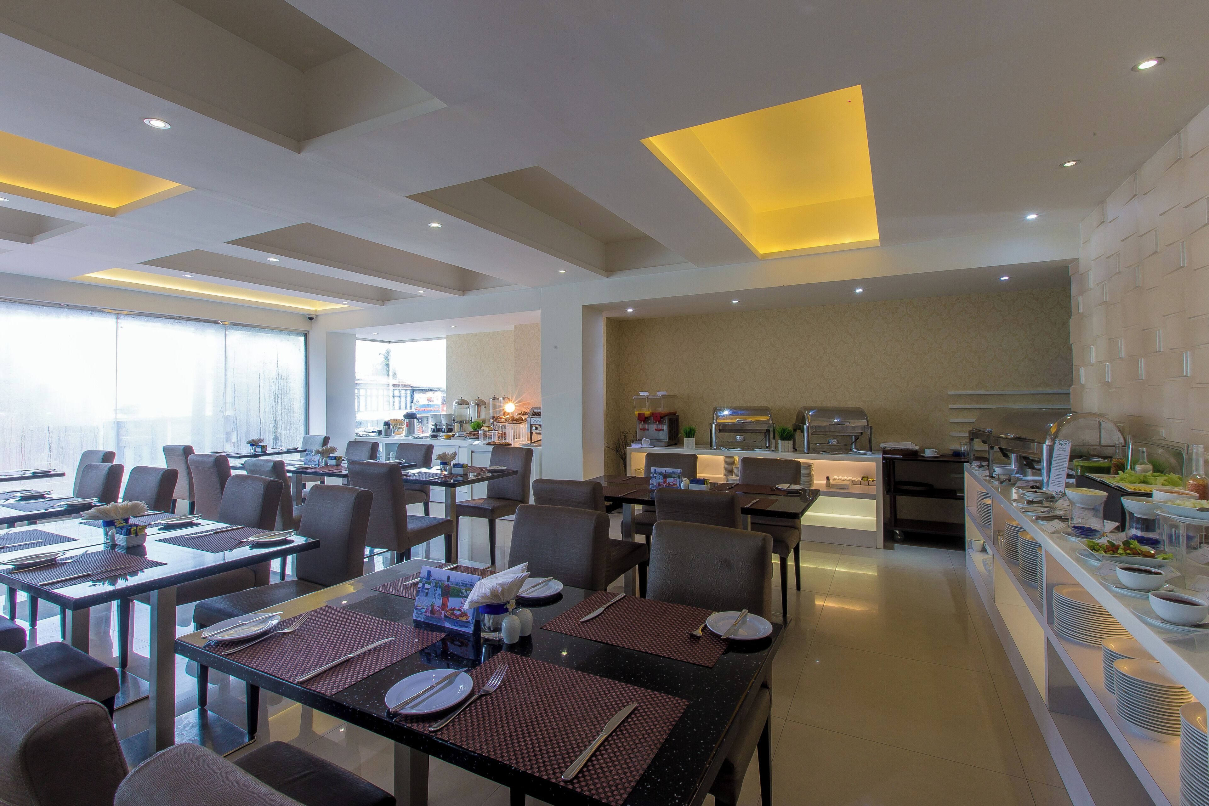 Un comedor moderno con varias mesas y sillas, una barra de buffet y una cocina al fondo.