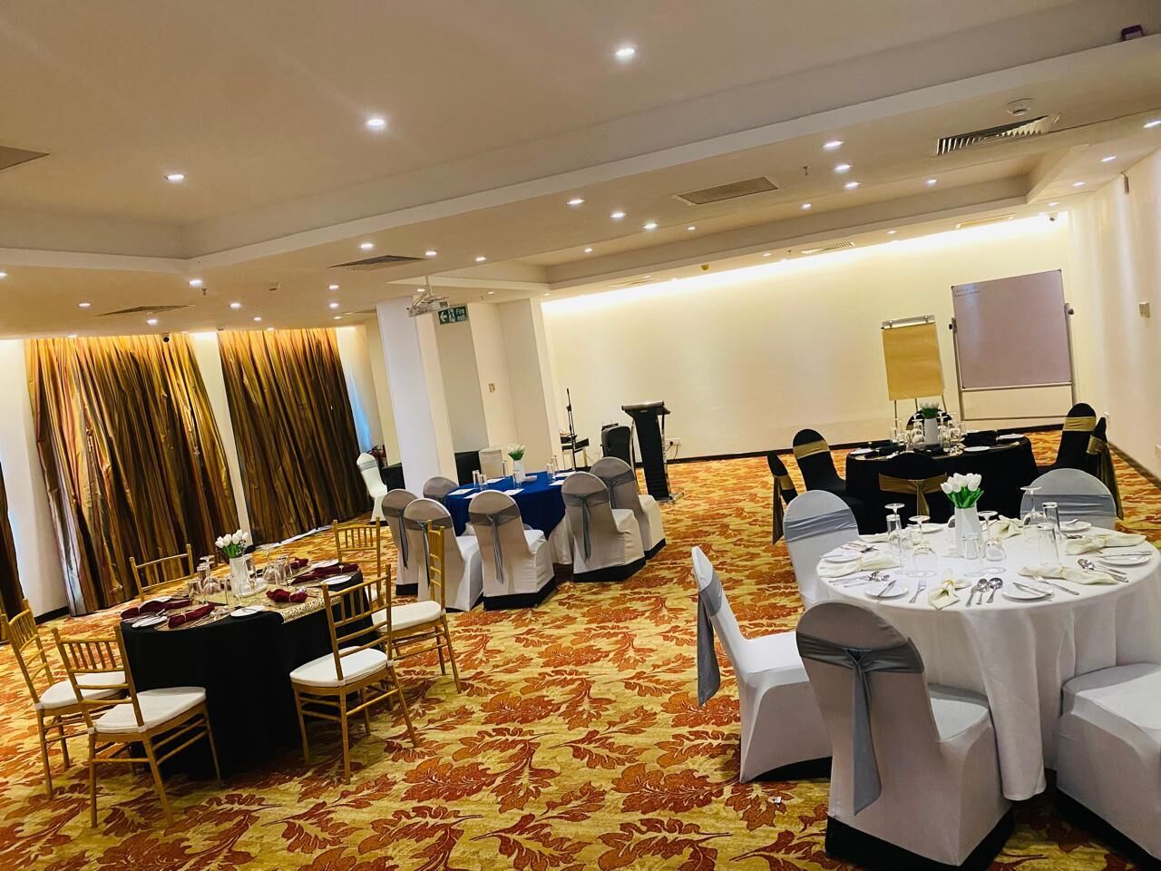 A banquet hall with round tables set for dining, white chairs, and a carpeted floor.