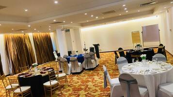 A banquet hall with round tables set for dining, white chairs, and a carpeted floor.