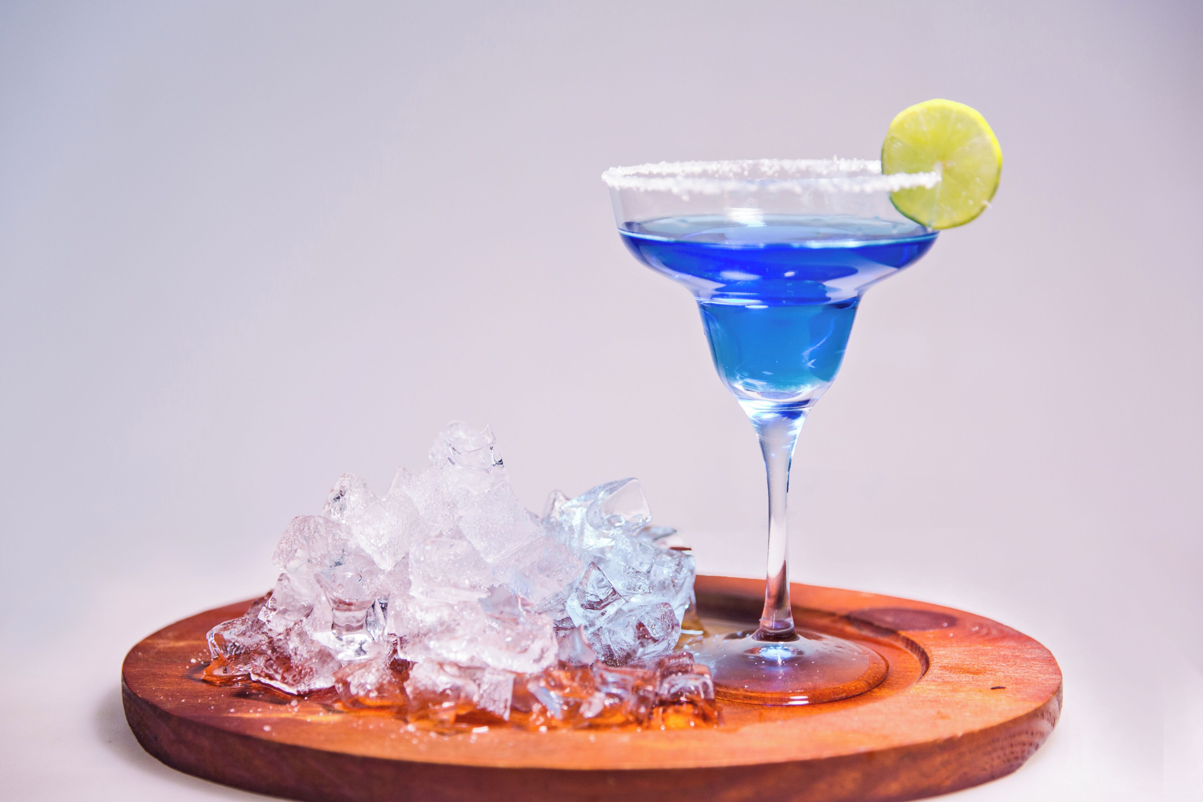 Un cocktail bleu, garni d’une tranche de citron vert, posé sur un sous-verre en bois.