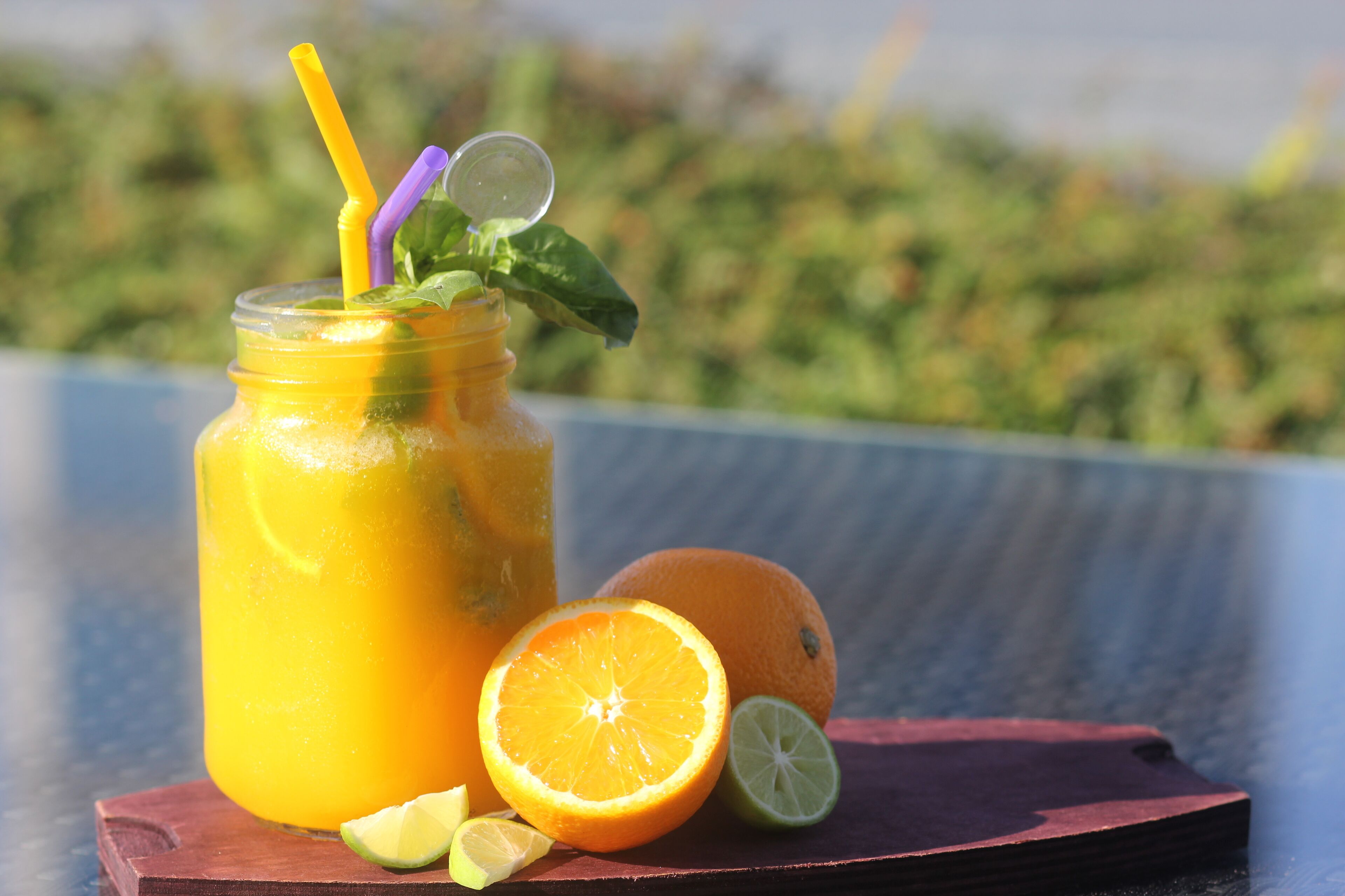 A glass of orange juice with a straw and mint leaves on a wooden table.