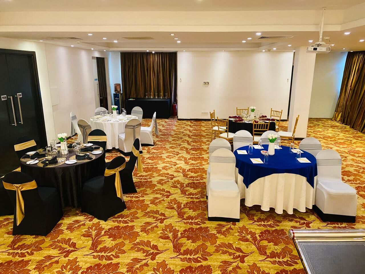 Un salón de conferencias con mesas redondas, sillas blancas y negras, y piso alfombrado.