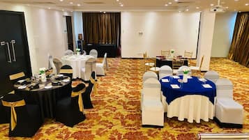 Un salón de conferencias con mesas redondas, sillas blancas y negras, y piso alfombrado.