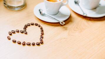 A table with two white cups of coffee, a spoon, and a heart-shaped arrangement of coffee beans.