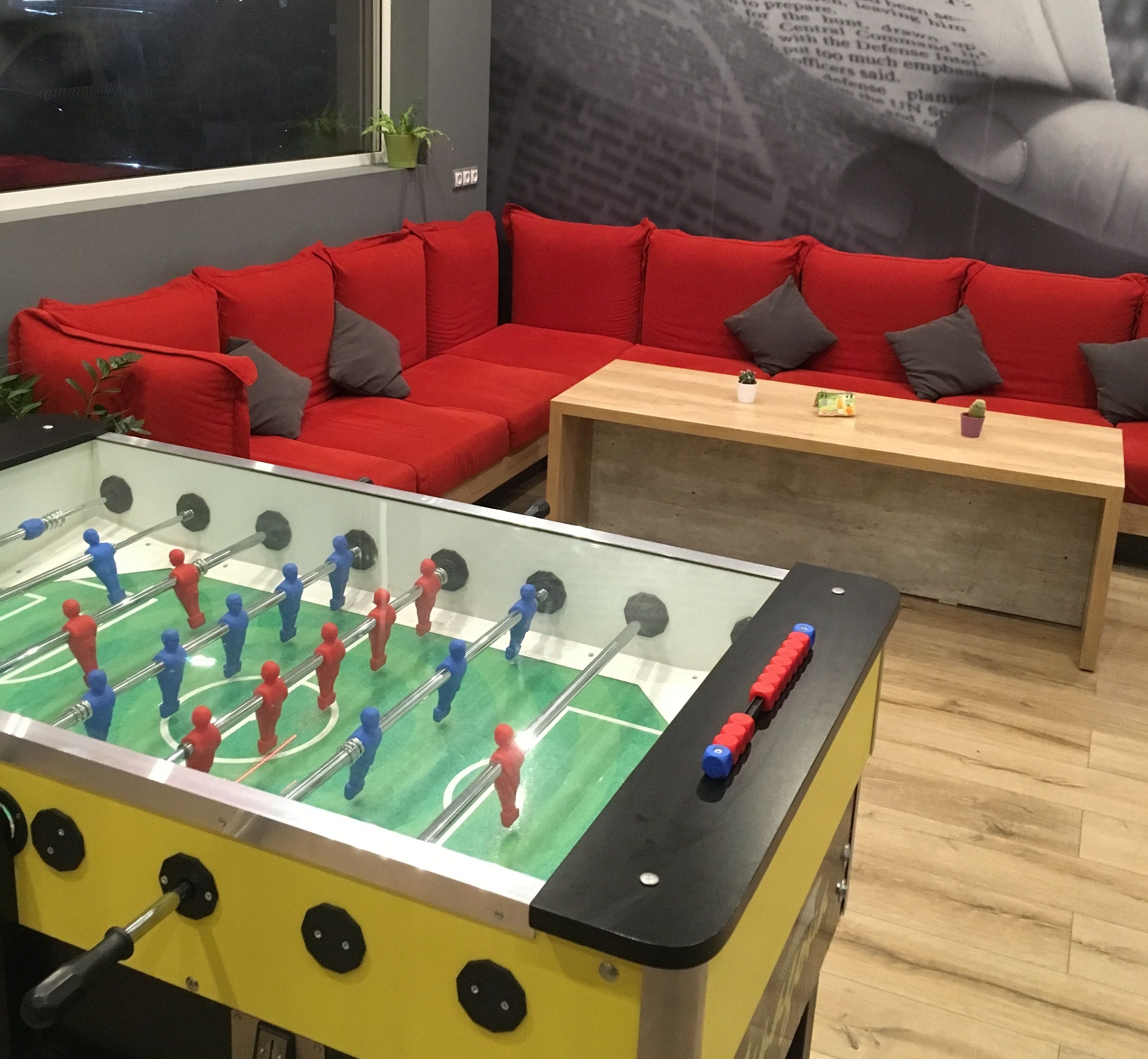 Una habitación con mesa de fútbol, un sofá rojo y una mesa de centro de madera.