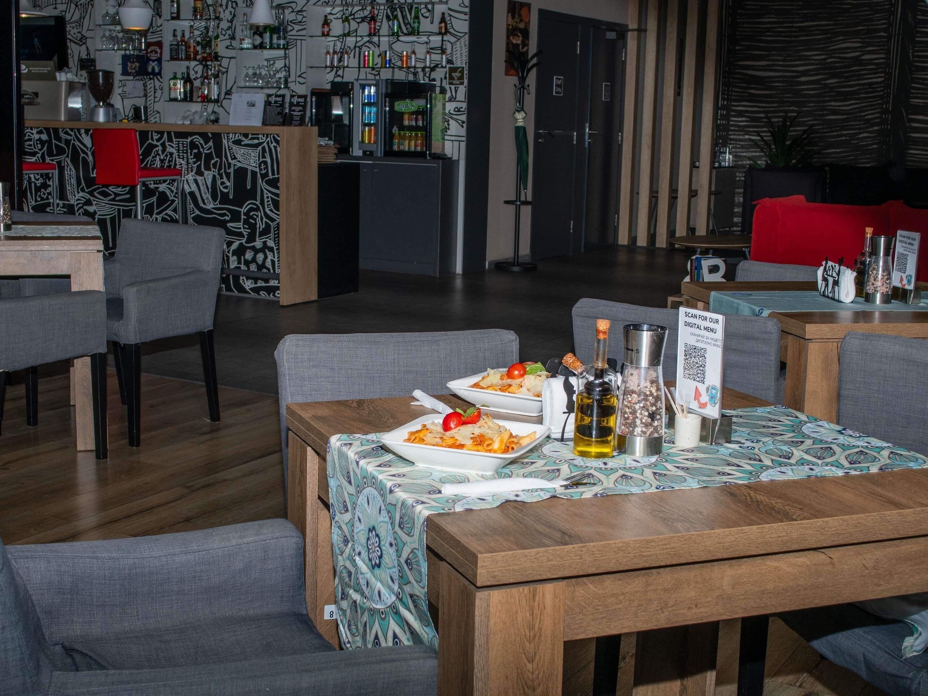 Un restaurante con área de bar, mesas y sillas de madera. Hay platos de comida sobre las mesas.