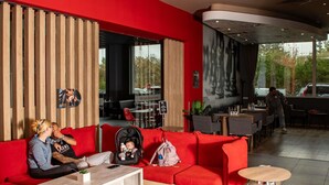 Un moderno vestíbulo de hotel con un sofá rojo, un panel de madera y un área de estar con mesas y sillas.