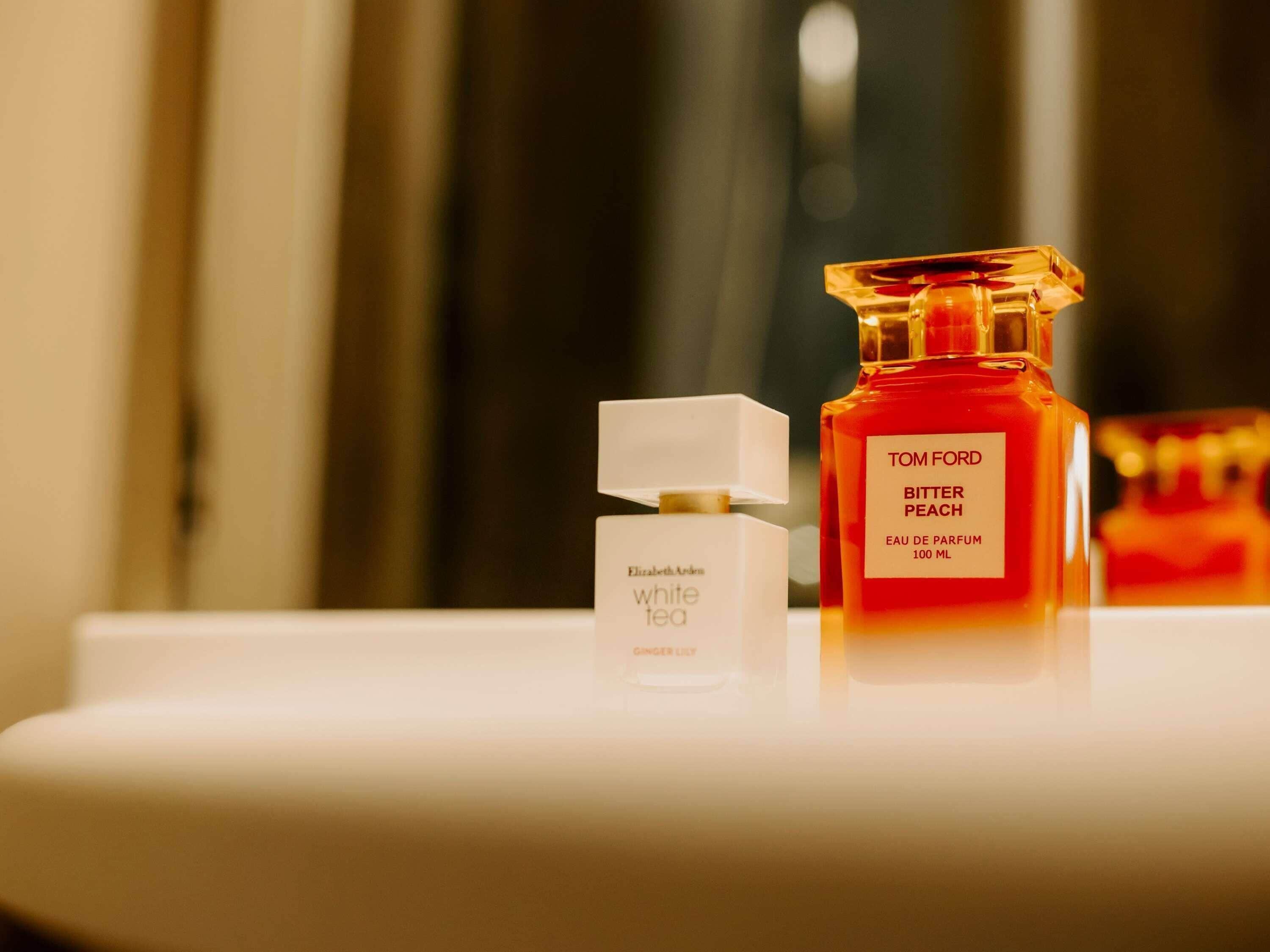 Een badkamer met een wit wastafel, een fles Tom Ford Bitter Peach parfum en een witte doos met de tekst Elizabeth Arden White Tea Ginger Lily.