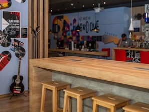 Un espace bar avec des tabourets en bois, une guitare et un mur ornĂ© de divers affiches et dâune fresque colorĂ©e.