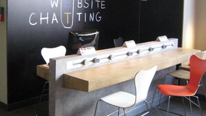 Un salón de conferencias moderno con una larga mesa, sillas blancas y rojas, e iluminación colgante.