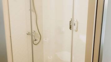 A glass-enclosed shower with a handheld showerhead, a wall-mounted soap dispenser, and a toilet paper holder on the wall.