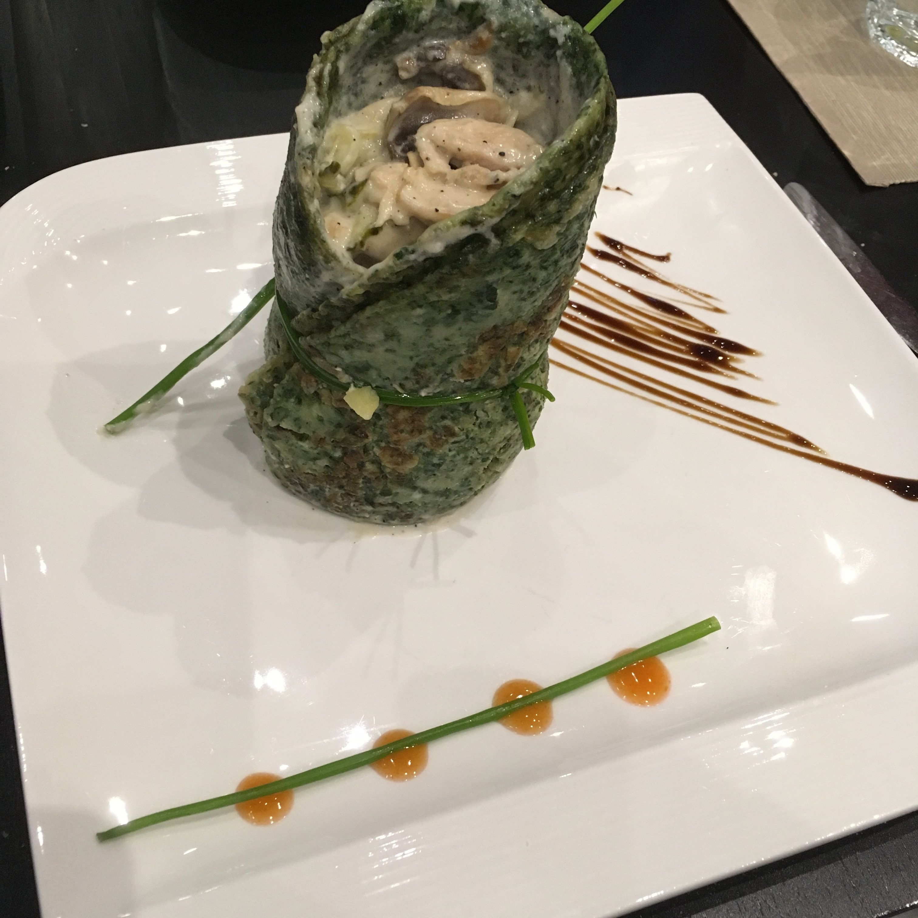 Un plato con un rollo de comida, posiblemente sushi o un wrap, decorado con salsa y un adorno verde.