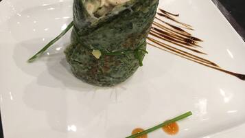 Un plato con un rollo de comida, posiblemente sushi o un wrap, decorado con salsa y un adorno verde.