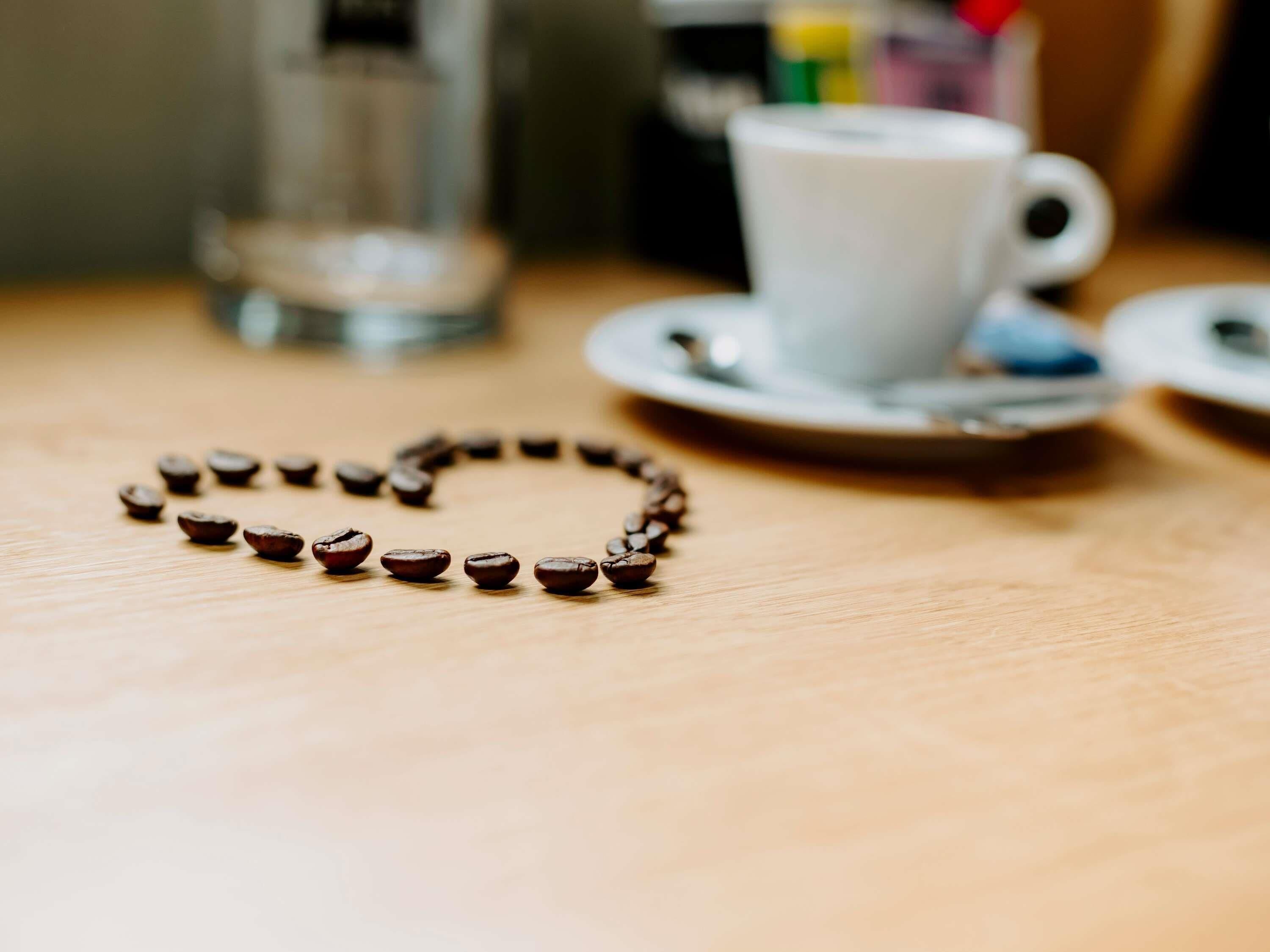 Een koffiekop op een schotel, met een hartvormige rangschikking van koffiebonen op tafel.