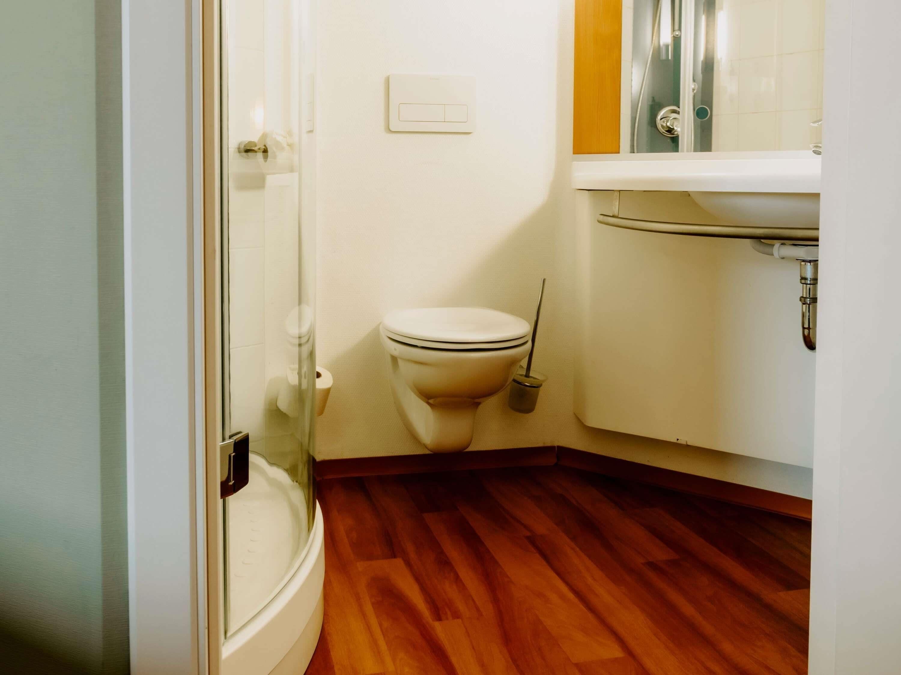 Un baño con inodoro, cabina de ducha de vidrio, lavabo y suelo de madera.