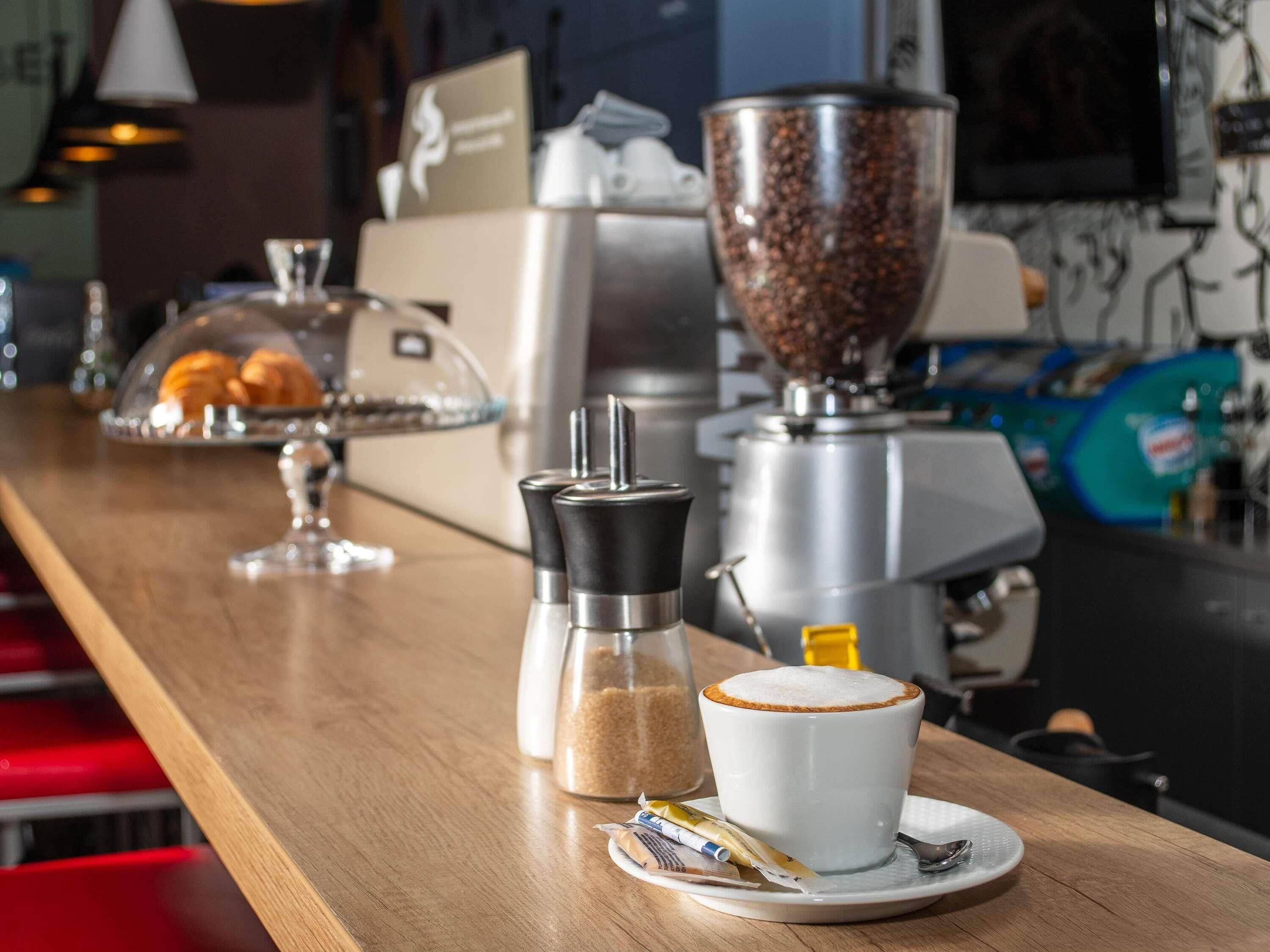 A coffee bar with a coffee machine, sugar and salt shakers, and a cup of coffee on a saucer.